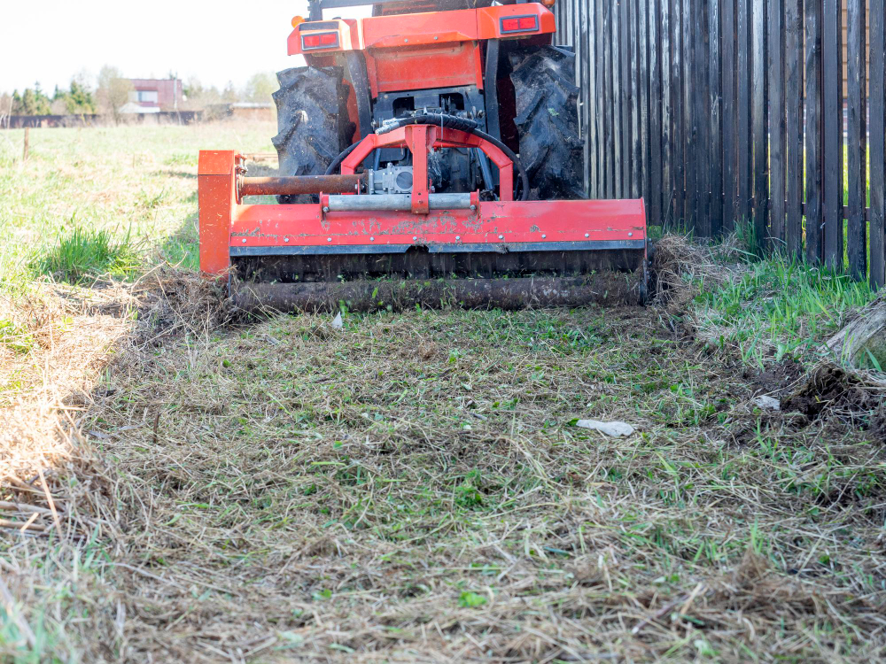 Débroussaillage de terrain – Devis rapide et conformité garantie 1 tracteur équipé d'une broyeuse de défrichage nettoyant un terrain en bordure de clôture
