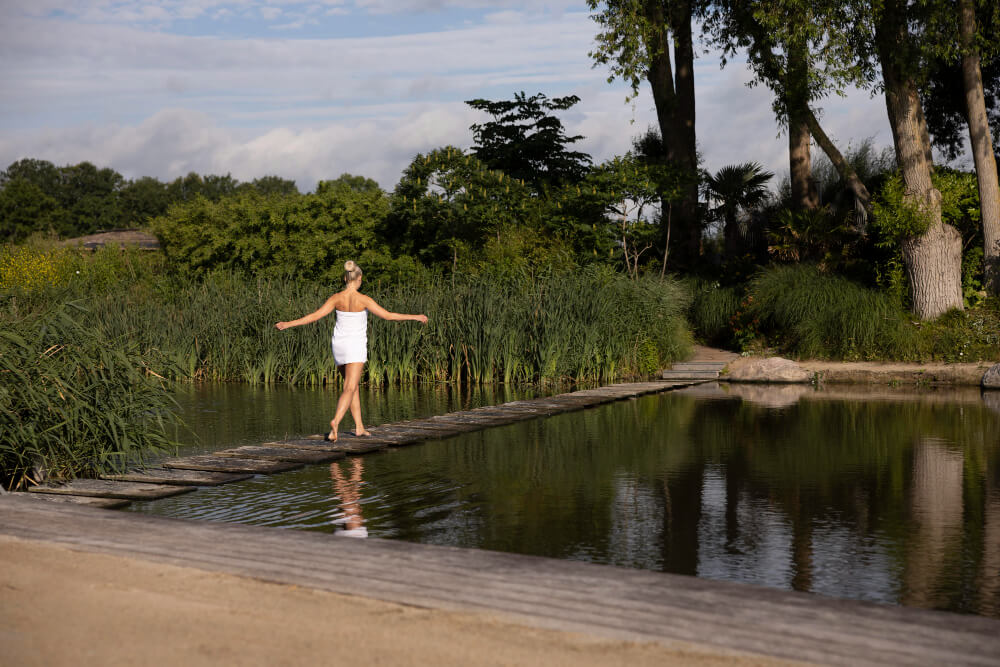 Bassin ou piscine : quel aménagement privilégier pour un jardin harmonieux ? 2 passerelle en bois traversant un bassin naturel paysager, ambiance bien-être et détente